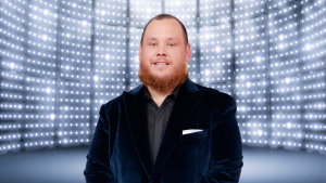 Luke Combs smiling in front of a bright background