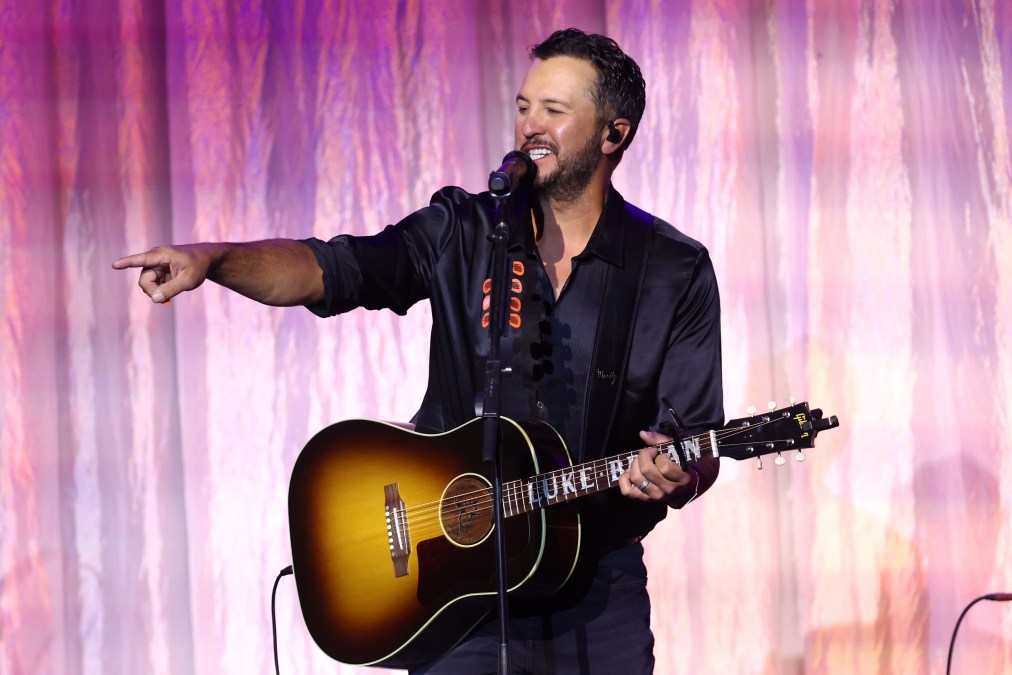Luke Bryan pointing to fans while holding a guitar.