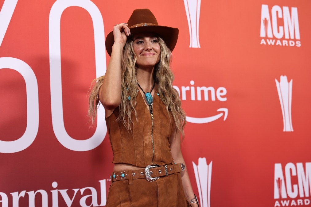 Lainey Wilson tipping her hat in front of a step and repeat.