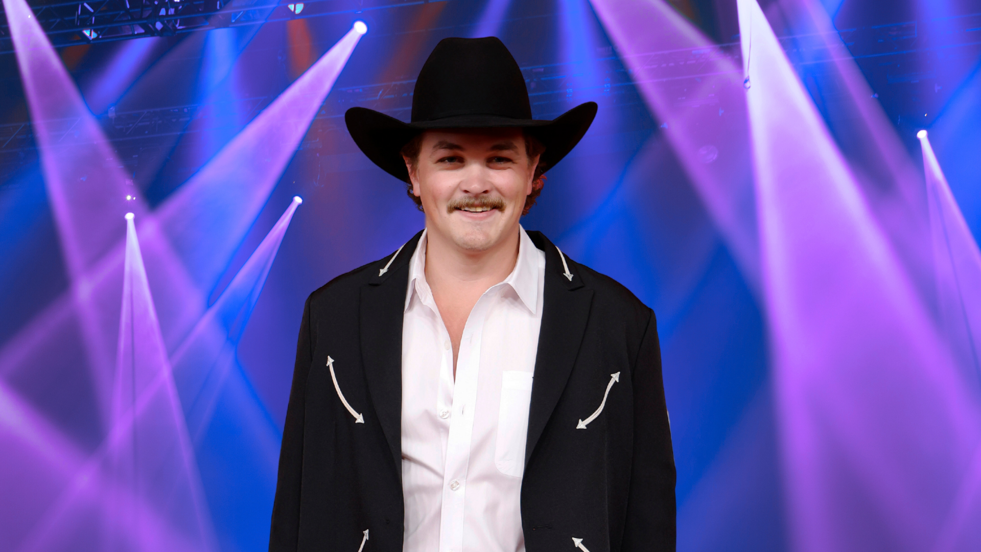 Zach Top posing in a cowboy hat in front of colorful lights.