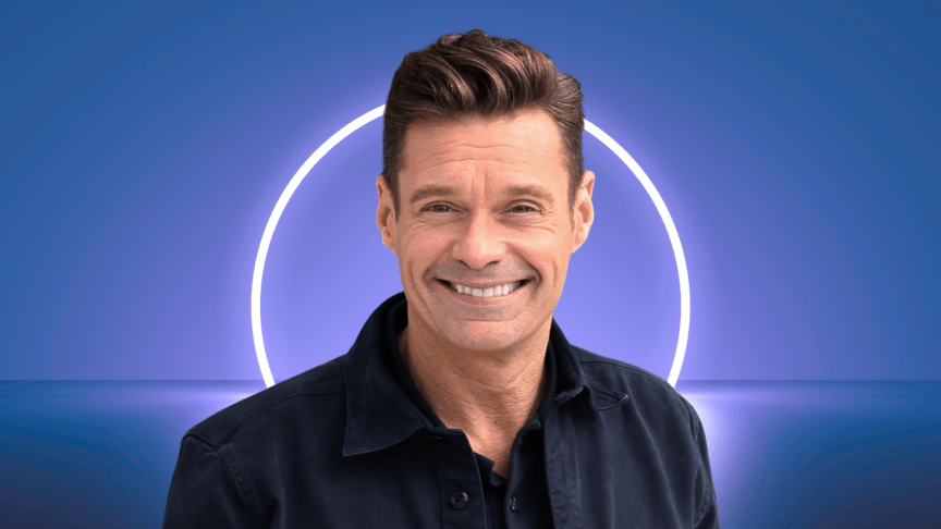 Ryan Seacrest smiling in front of a white light.