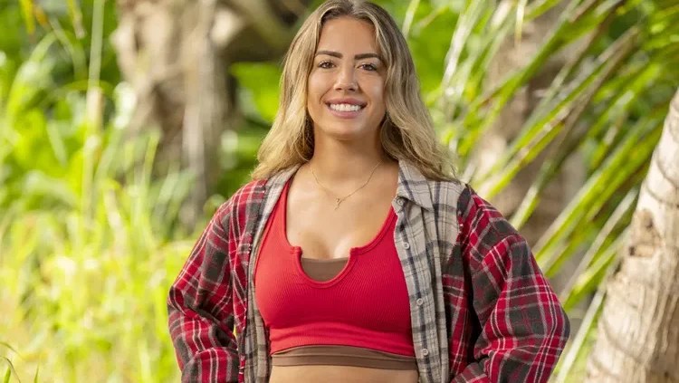 Dee Valladares smiling on “Survivor 50” in red top and plaid shirt